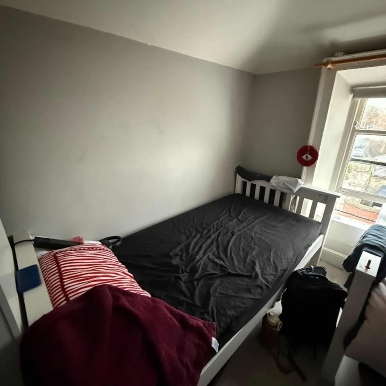 Small bedroom with a single bed, red striped pillow, and gray walls by a window.