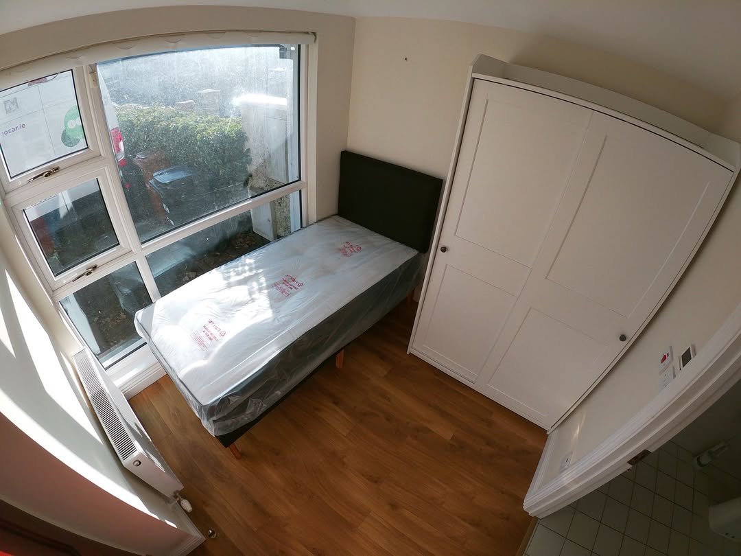 Small bedroom with single bed, wardrobe, and window. Natural light.