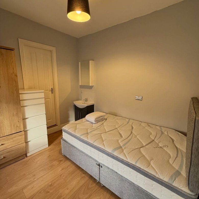 Small bedroom with single bed, wardrobe, and sink. Neutral color scheme.