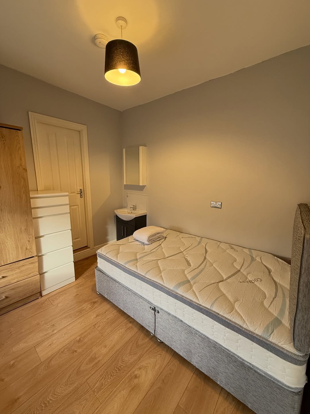 Small bedroom with single bed, wardrobe, and sink. Neutral color scheme.