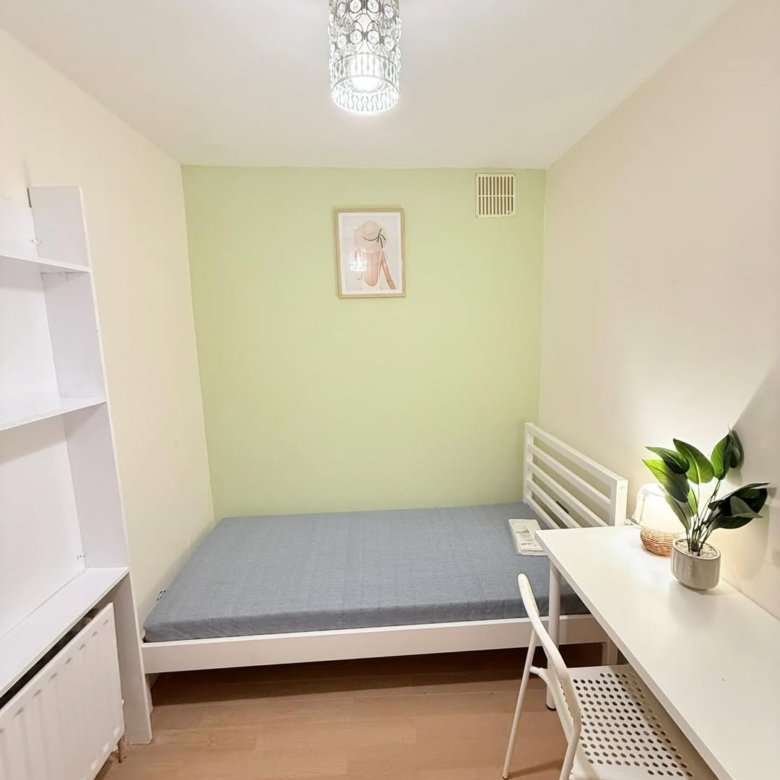 Small bedroom with single bed, desk, and white furniture against a light green wall.