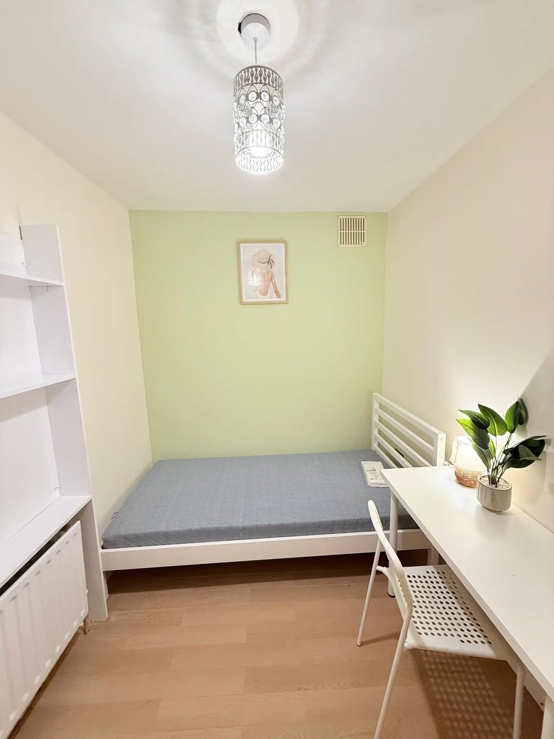 Small bedroom with single bed, desk, and white furniture against a light green wall.