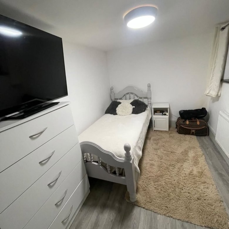 Cozy bedroom with single bed, white dresser, rug, and TV.