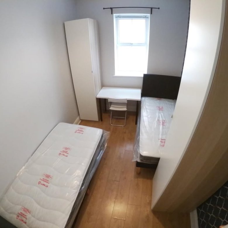 Small bedroom with two twin beds, desk, wardrobe, and window.