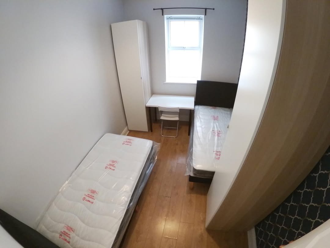 Small bedroom with two twin beds, desk, wardrobe, and window.