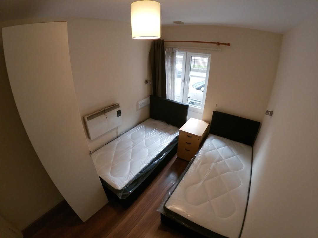 Small bedroom with two twin beds, bedside table, and window.