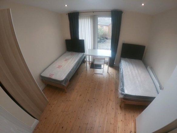 Small bedroom with two beds, desk, and window. Simple, furnished interior.