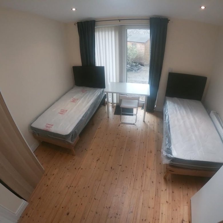 Small bedroom with two beds, desk, and window. Simple, furnished interior.