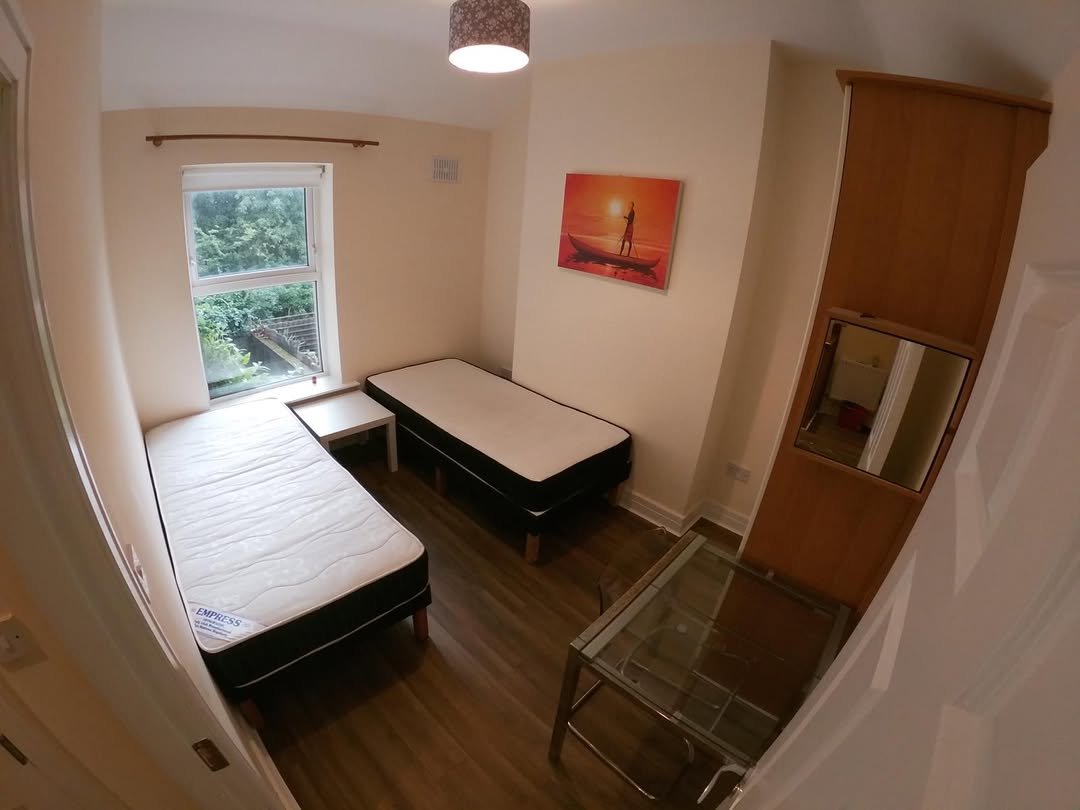 Cozy bedroom with two beds, desk, mirror, and artwork.