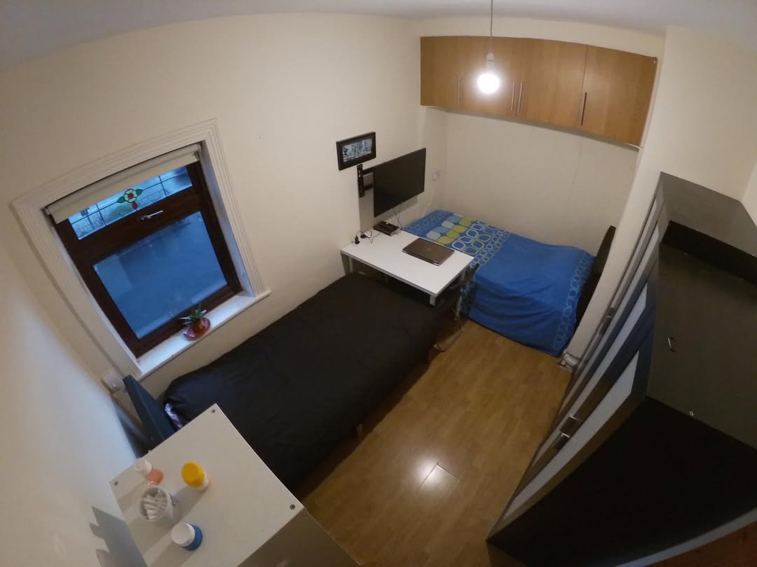 Small bedroom with two beds, desk, and storage cabinets. Compact living space.