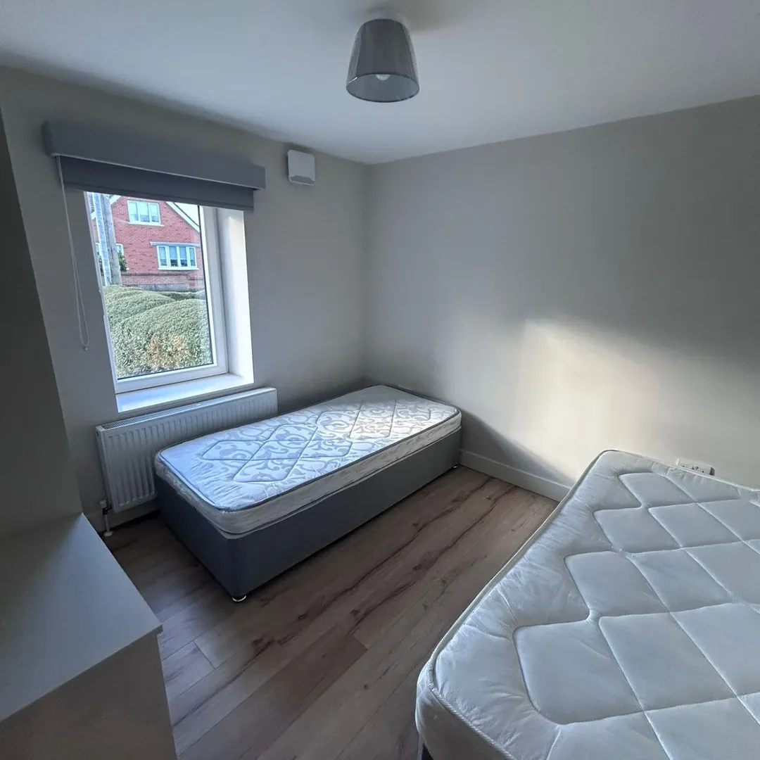 Small bedroom with two single beds, window with blinds, and light wood flooring.