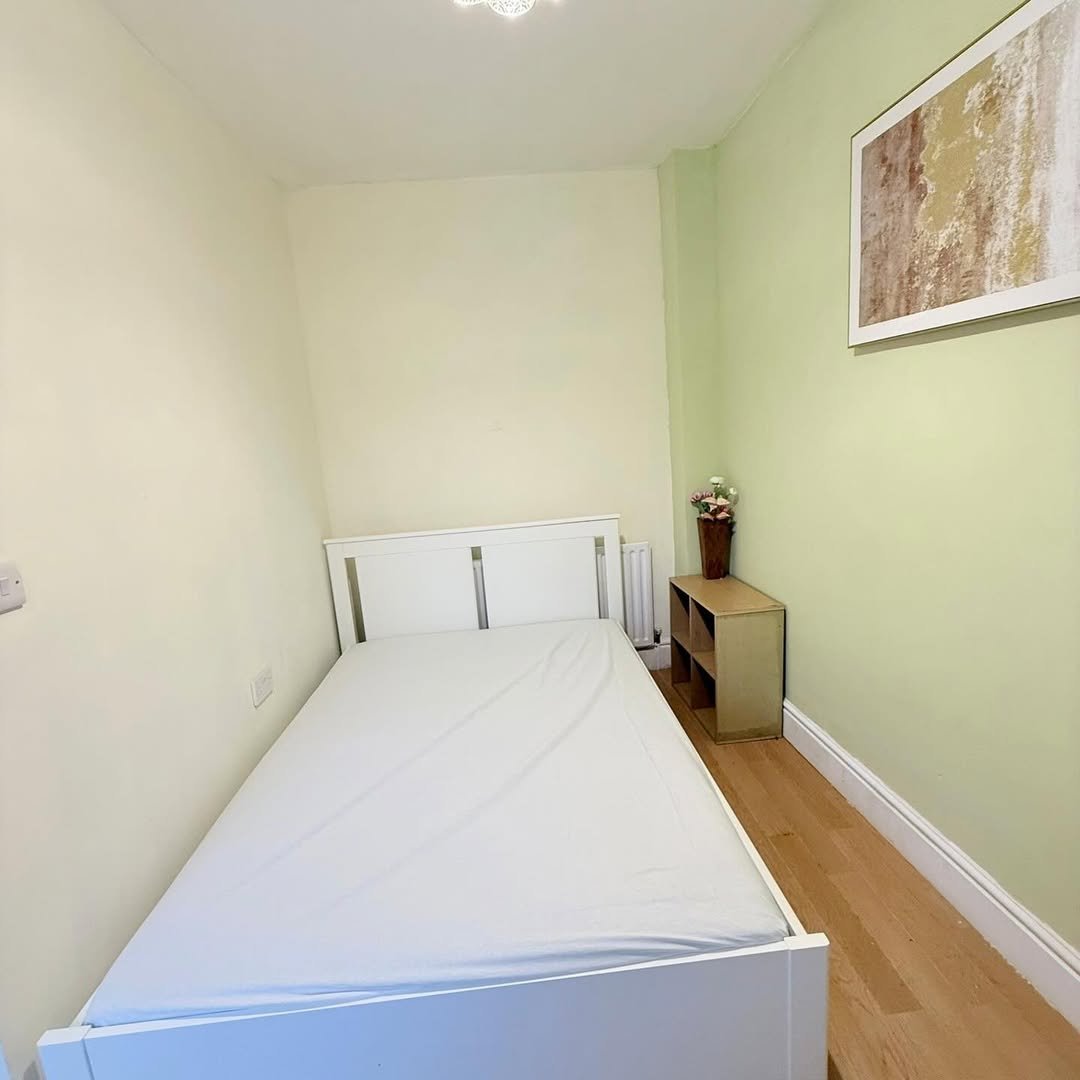 Small bedroom with white bed, bedside table, and light green walls.