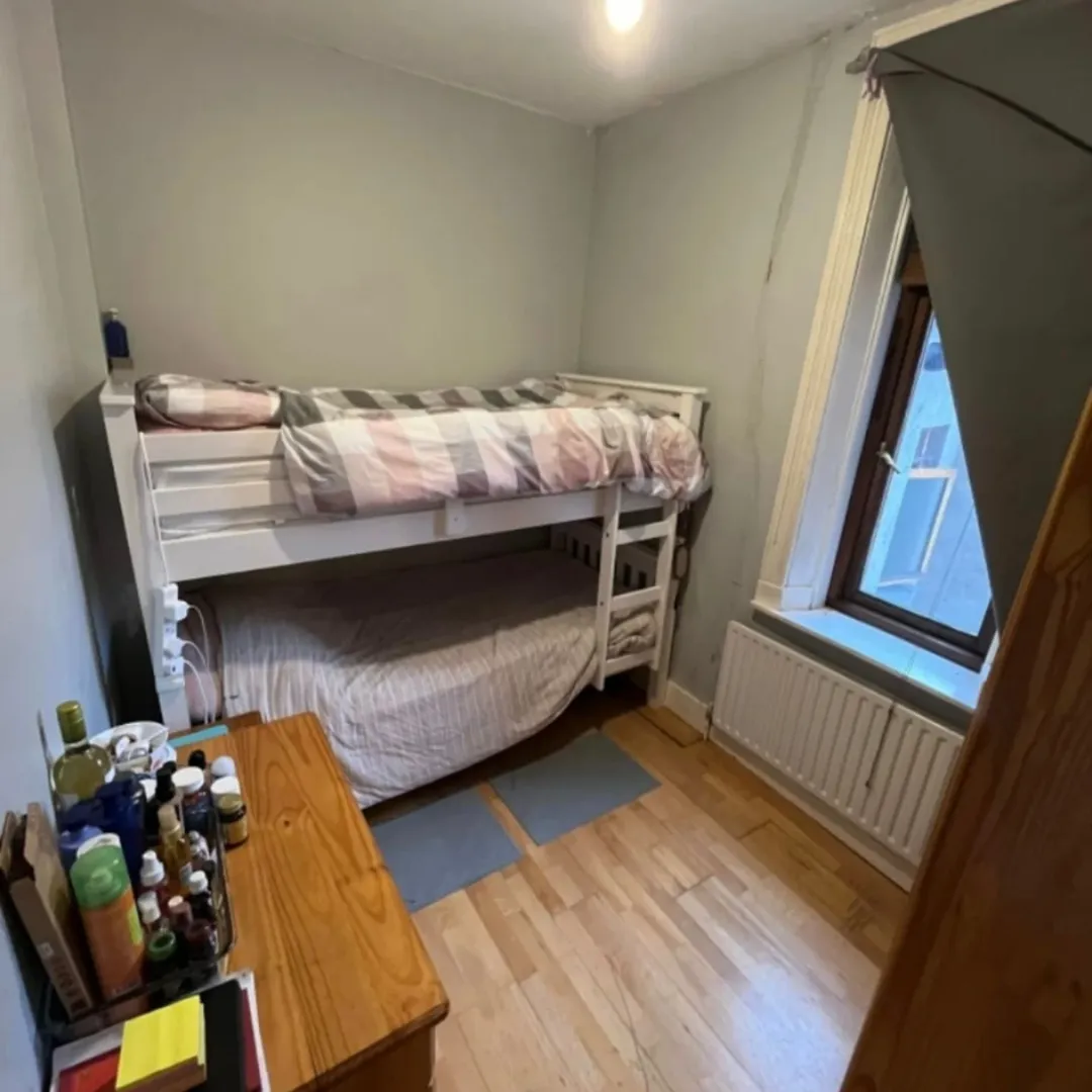 Small bedroom with white bunk beds, wooden floors, and a window.