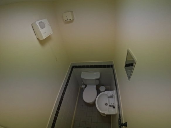Small, simple bathroom with toilet, sink, mirror, and hand dryer in a compact space.