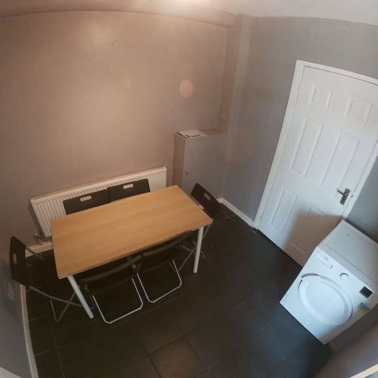 Small dining area with table, chairs, radiator, washing machine, and door in a room with gray walls and dark floor.