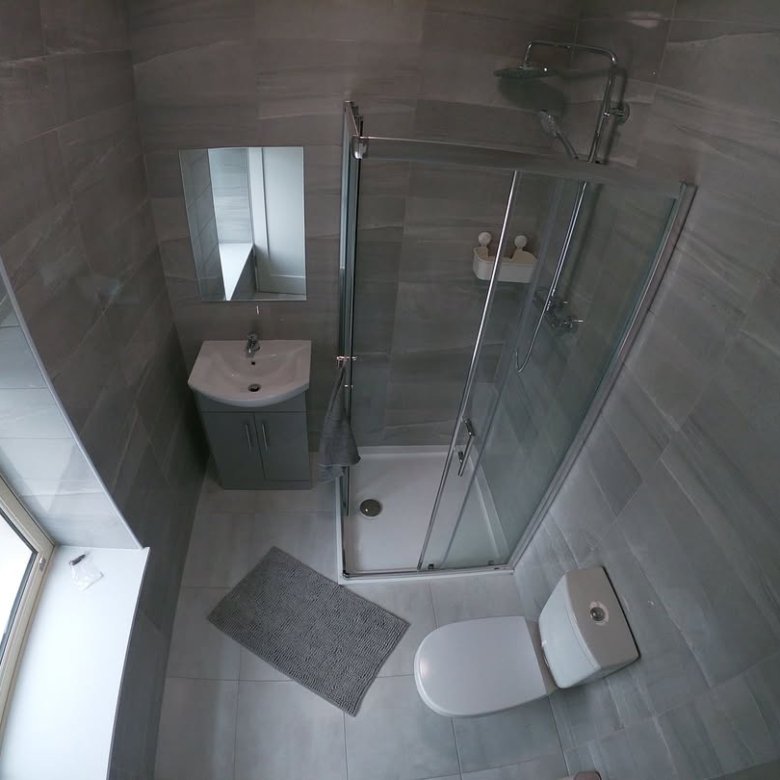 Small gray bathroom with shower, toilet, sink, window, and gray tile. Modern, compact bathroom design.