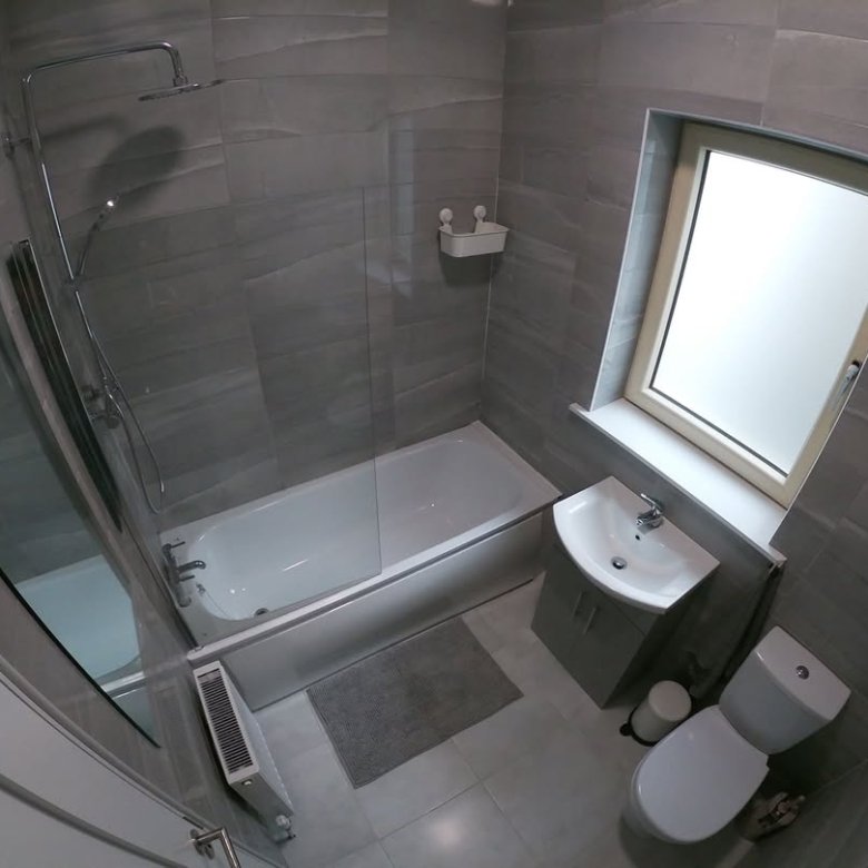 Small gray bathroom with tub, shower, toilet, and sink under window.