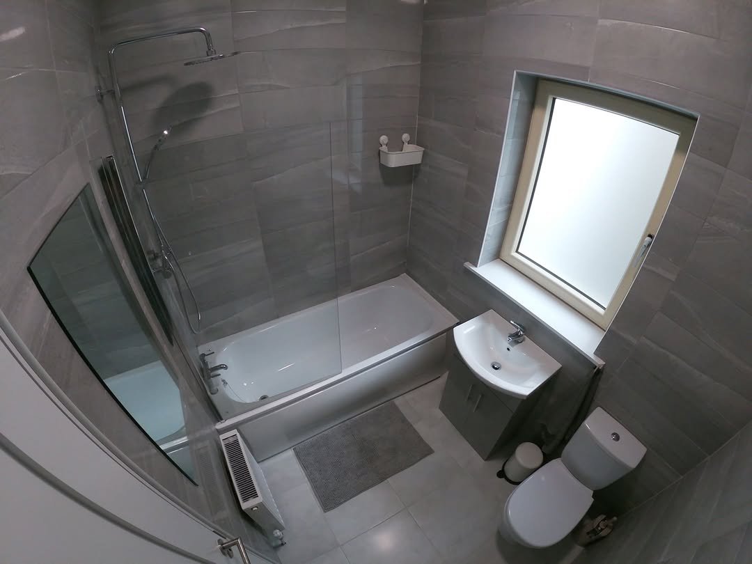 Small gray bathroom with tub, shower, toilet, and sink under window.