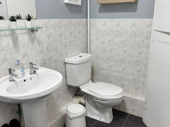 Small gray bathroom with white fixtures: toilet, sink, shelves, and mirror.
