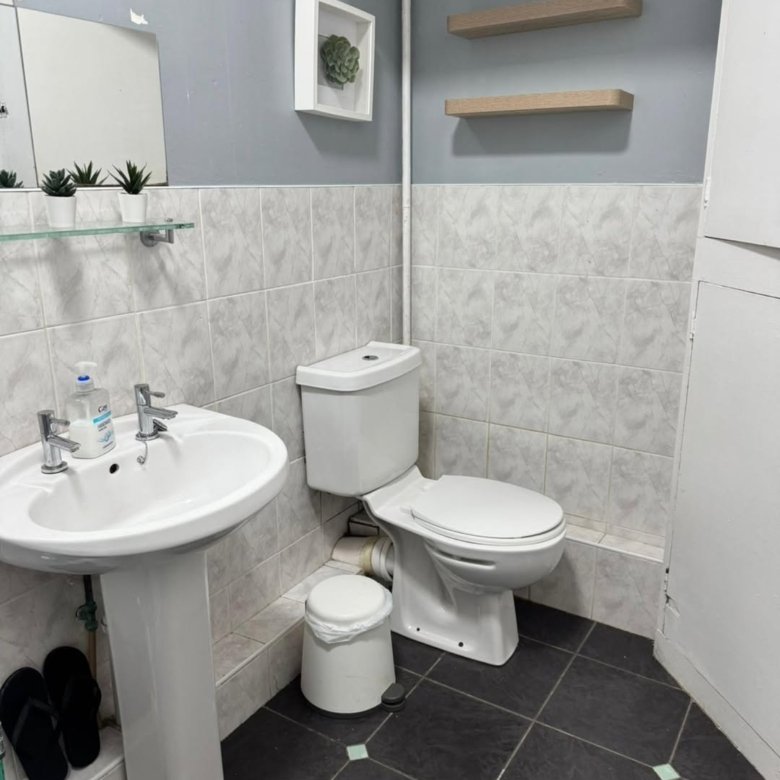 Small gray bathroom with white fixtures: toilet, sink, shelves, and mirror.