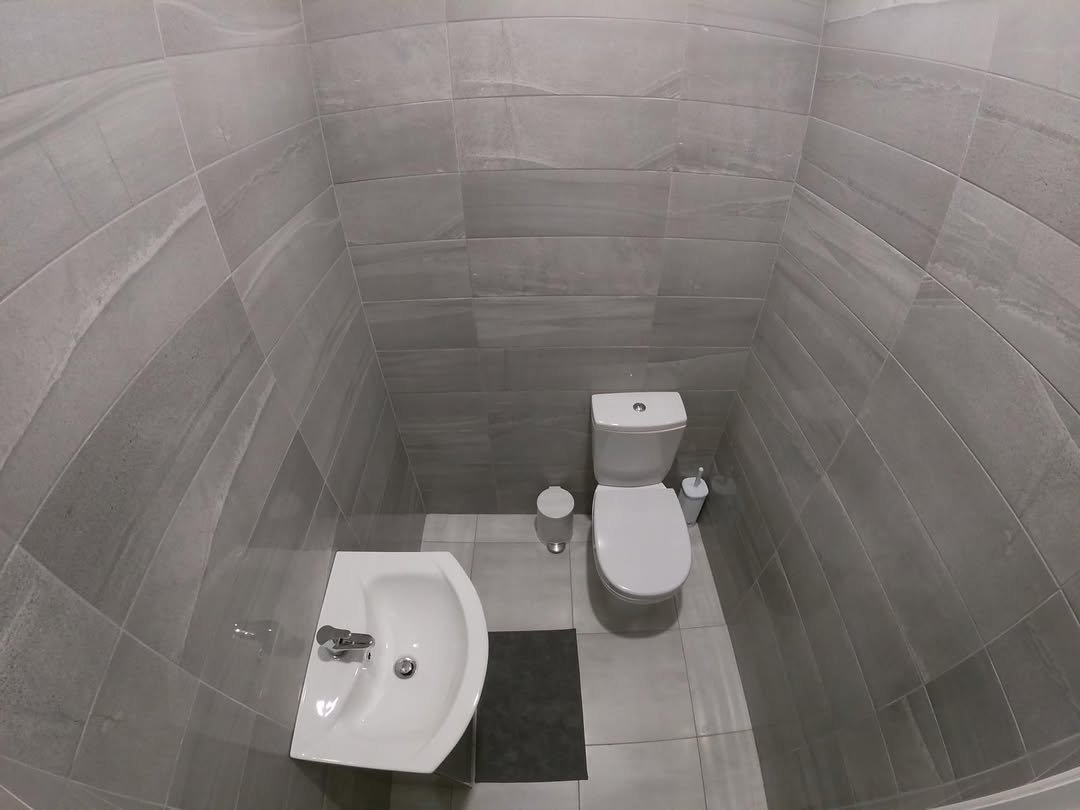 Small gray tiled bathroom with toilet and sink.