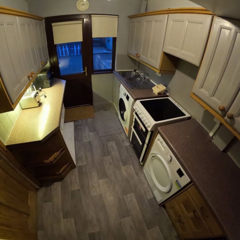 Small kitchen with gray cabinets, brown countertops, washing machine, and oven, viewed with a fisheye lens.