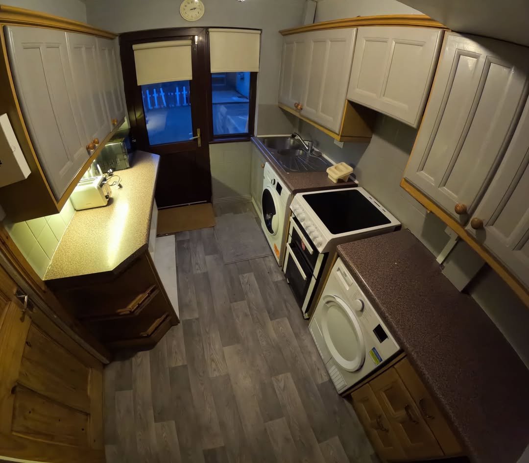 Small kitchen with gray cabinets, brown countertops, washing machine, and oven, viewed with a fisheye lens.
