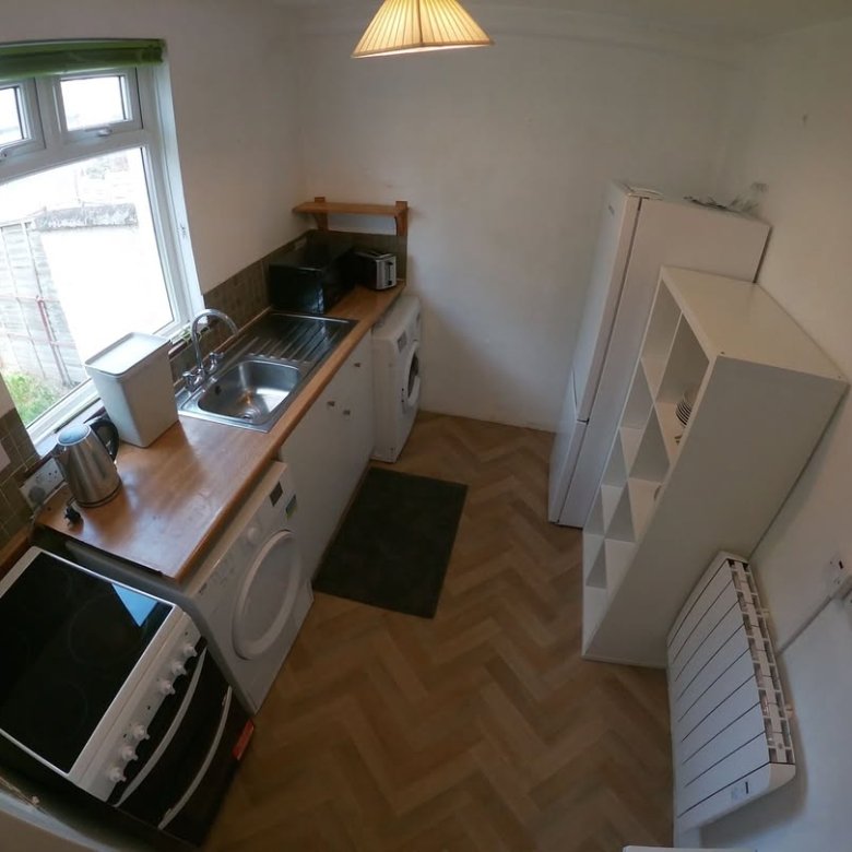 Compact kitchen with white appliances, wood countertop, and herringbone floor.