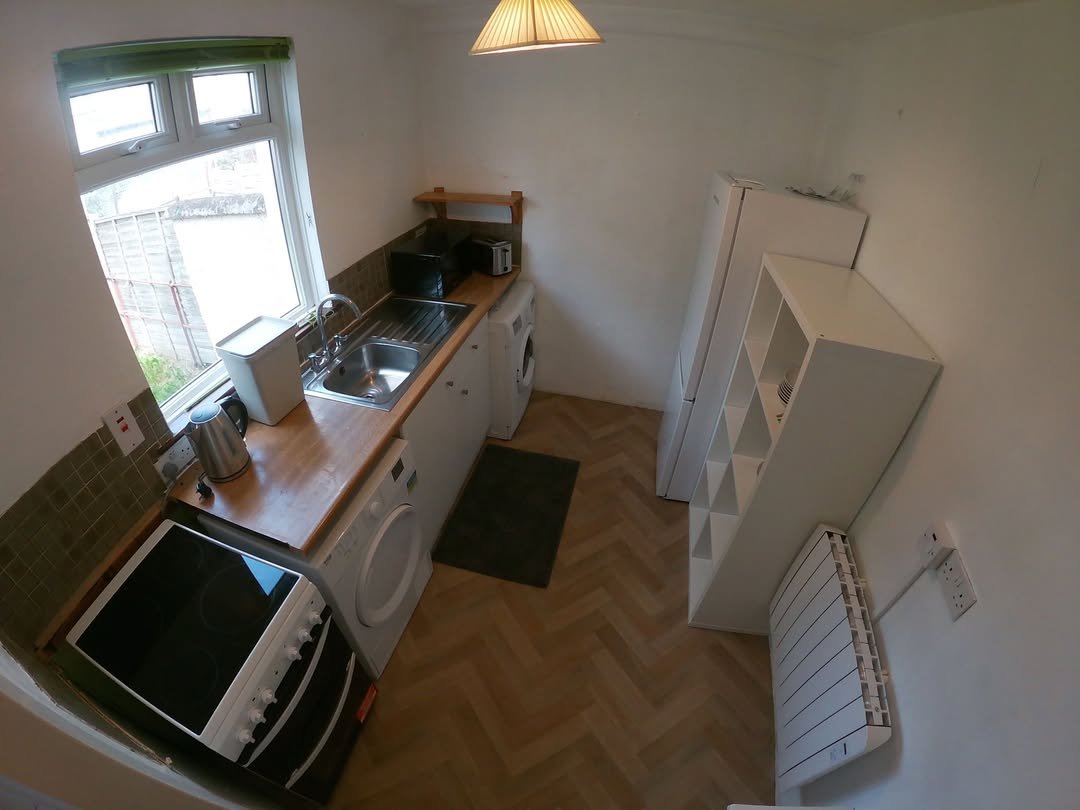 Compact kitchen with white appliances, wood countertop, and herringbone floor.