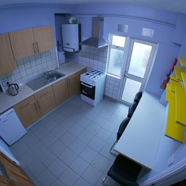 Compact kitchen with white appliances, light wood cabinets, and yellow shelving.