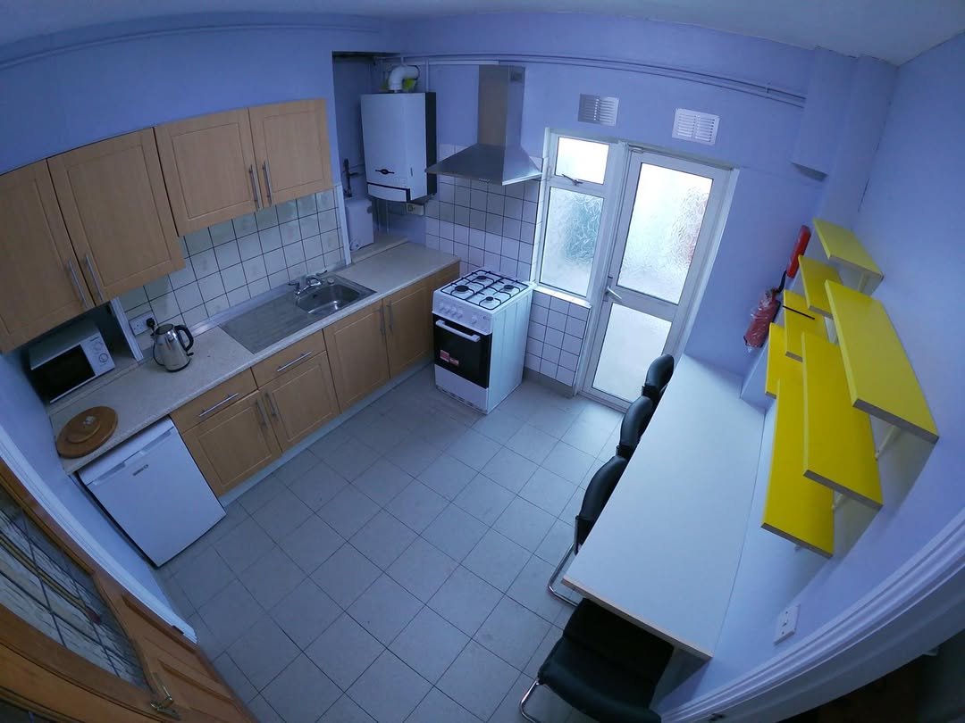 Compact kitchen with white appliances, light wood cabinets, and yellow shelving.