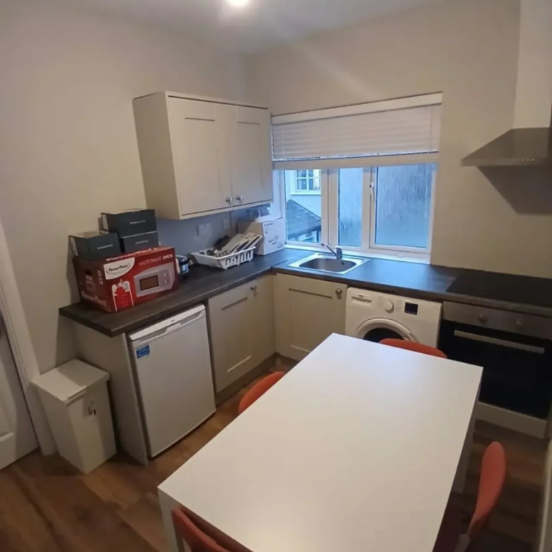 Compact kitchen with white cabinets, table, and appliances under a window.