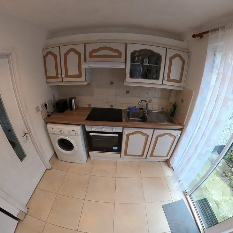 Compact kitchen with white cabinets, washing machine, and garden view through glass door.