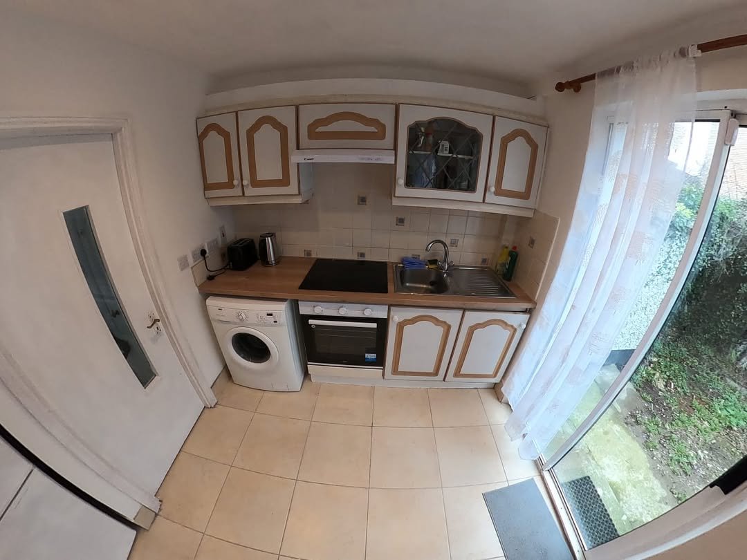 Compact kitchen with white cabinets, washing machine, and garden view through glass door.