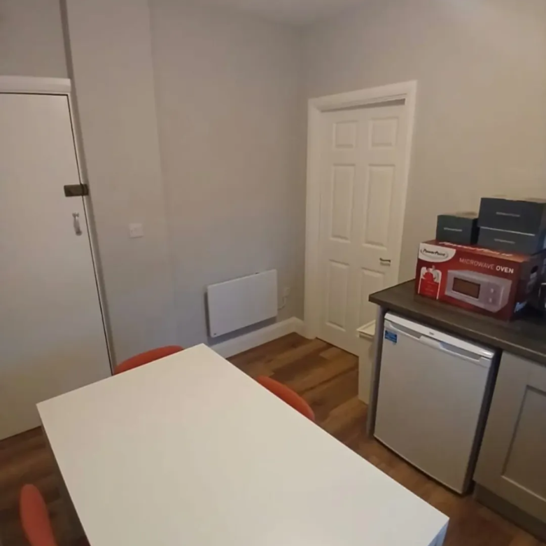 Small kitchen with white table, mini fridge, microwave oven box, and orange chairs.