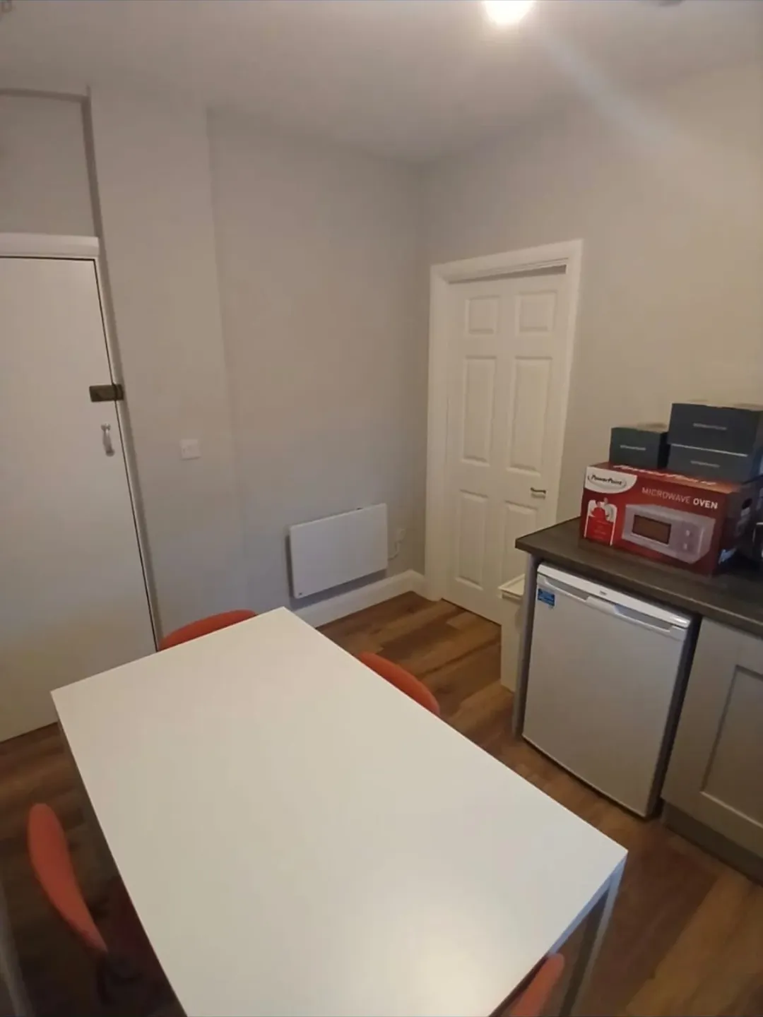 Small kitchen with white table, mini fridge, microwave oven box, and orange chairs.
