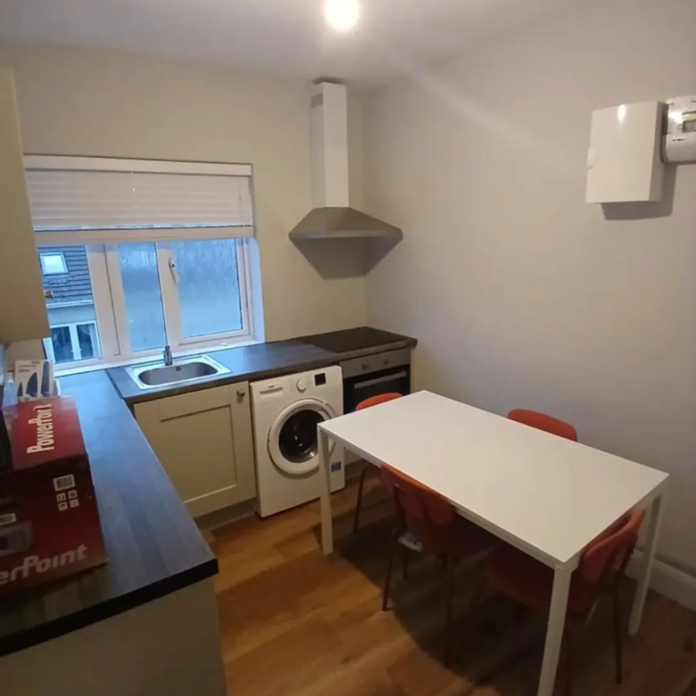 Compact kitchen with white table, orange chairs, and washing machine.