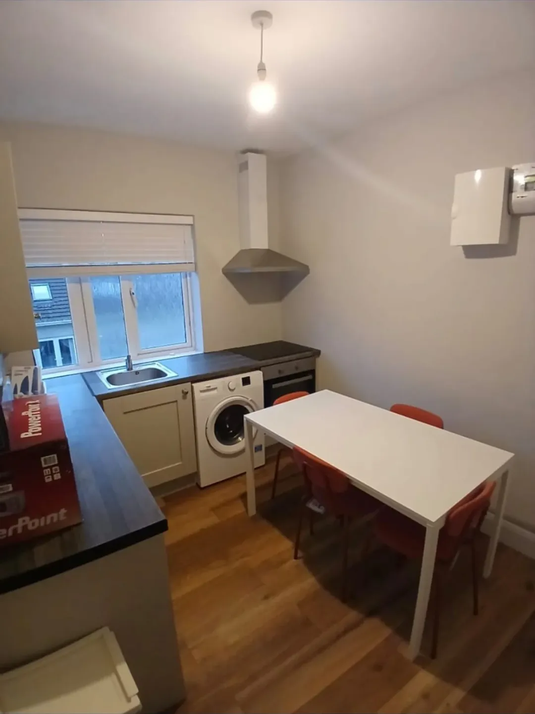 Compact kitchen with white table, orange chairs, and washing machine.