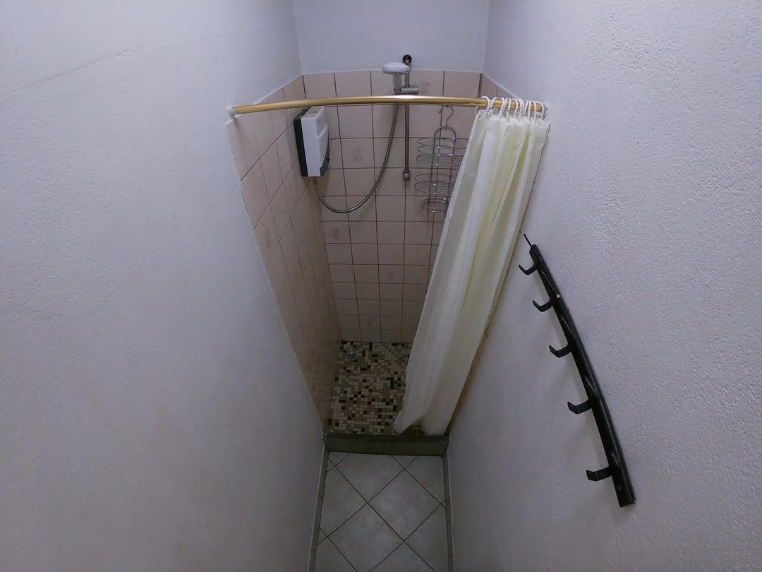 Small, oddly shaped shower with curtain and wall-mounted hooks in a bathroom.