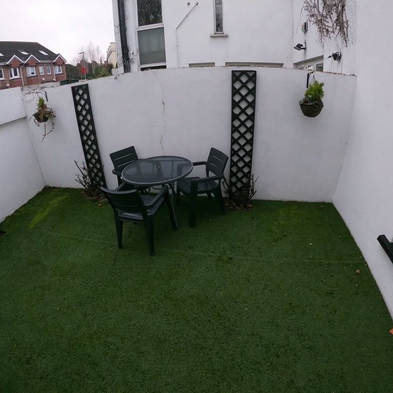 Small outdoor patio with artificial grass, table, and chairs.