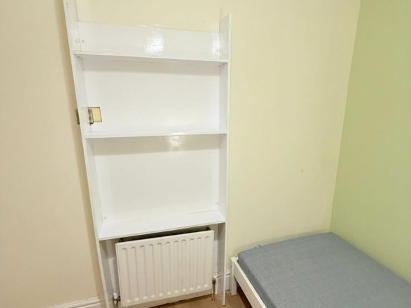 Small room with white shelving unit, radiator, and single bed against light yellow and green walls.