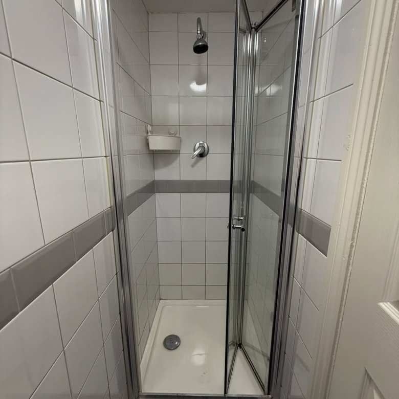 Small shower stall with folding glass door and white tile walls.