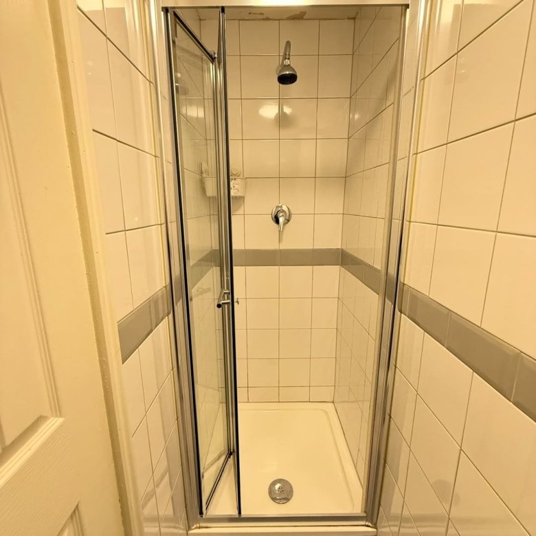 Small shower stall with glass door ajar, white tiled walls.