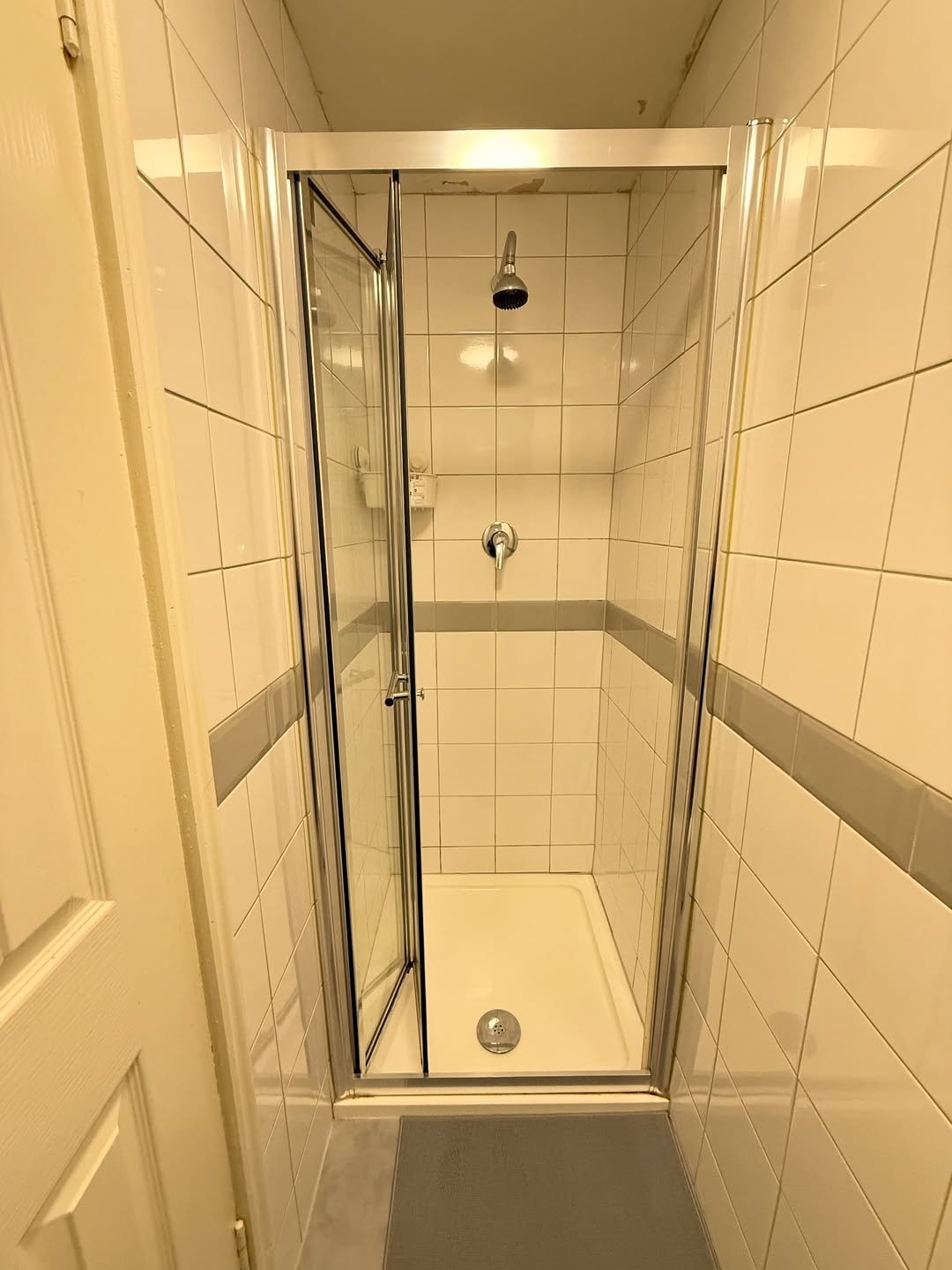 Small shower stall with glass door ajar, white tiled walls.