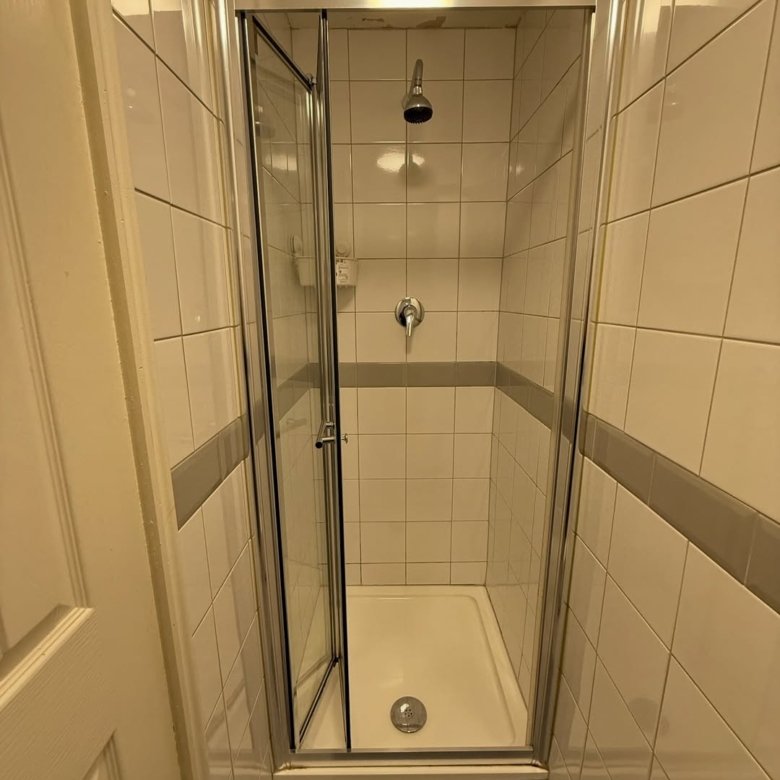 Small tiled shower stall with open glass door.