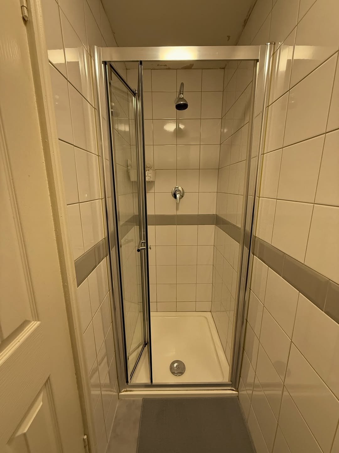 Small tiled shower stall with open glass door.