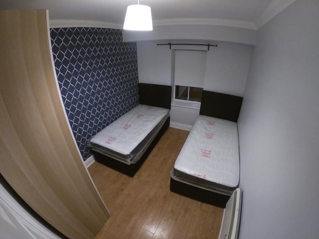 Small bedroom with two twin beds, blue wallpaper, and wood flooring.