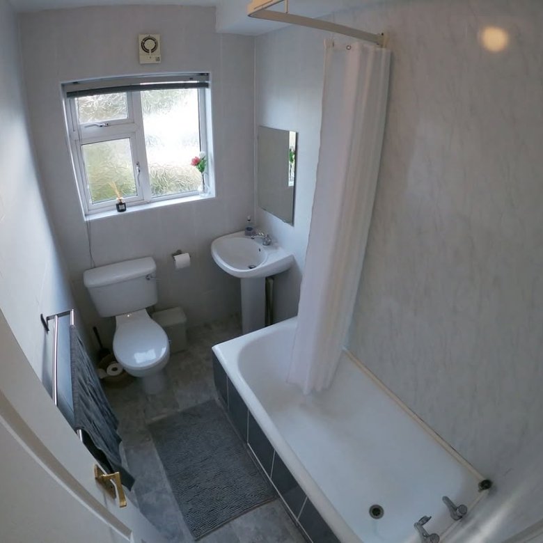 Small bathroom with white tub, toilet, sink, and gray floor mat.