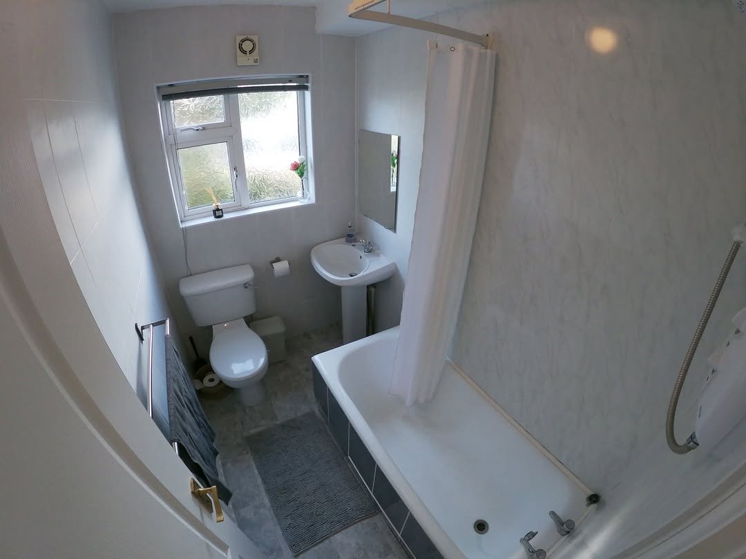 Small bathroom with white tub, toilet, sink, and gray floor mat.
