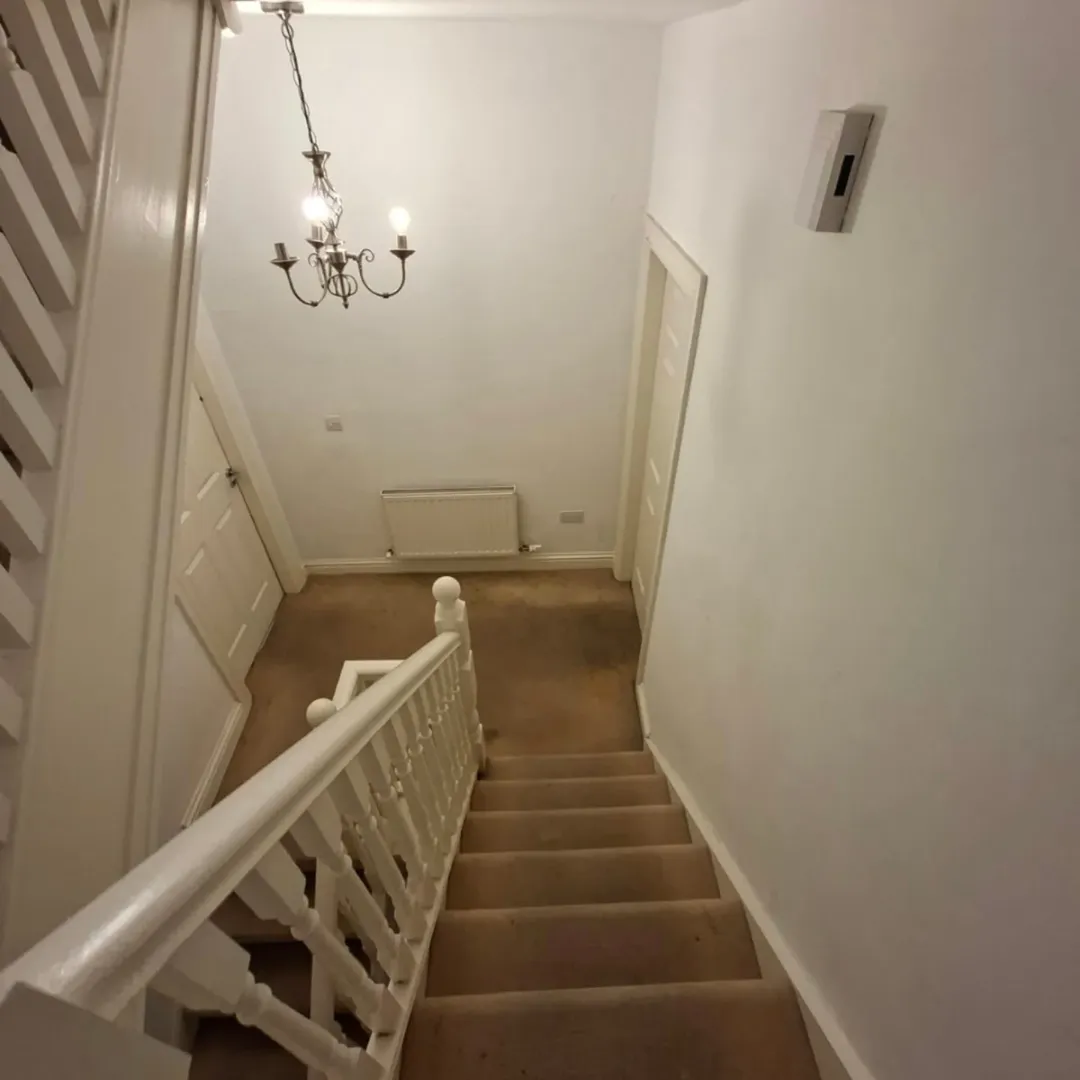 Staircase with white railing leading to landing with chandelier and doors.